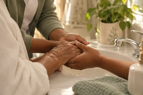 A caregiver steadying an older person’s hands at a sink